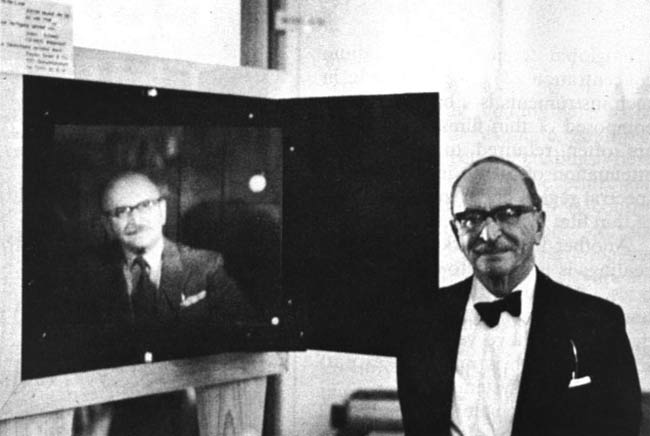 Dr. Dennis Gabor, winner of the 1971 Nobel Prize for physics, stands beside a portrait hologram made by McDonnell Douglas Electronics. Courtesy of McDonnell Douglas Electronics.